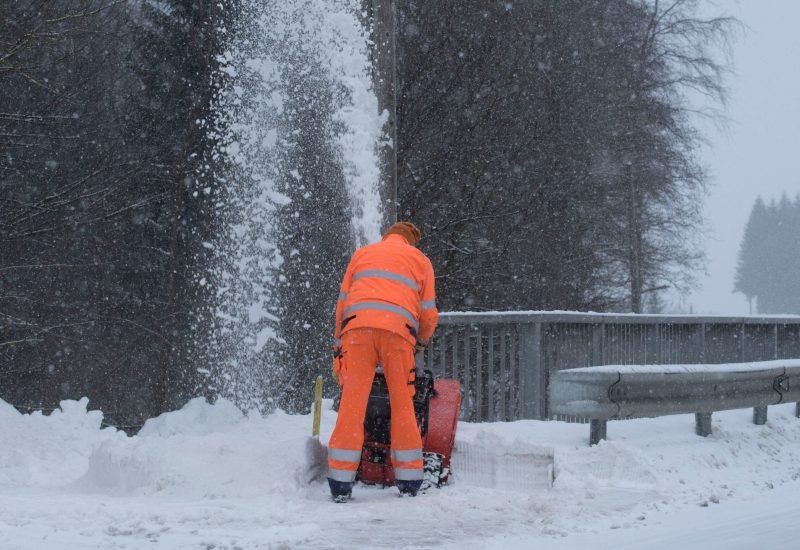 a professional wearing an orange suit removing snow using a snow removal machine
