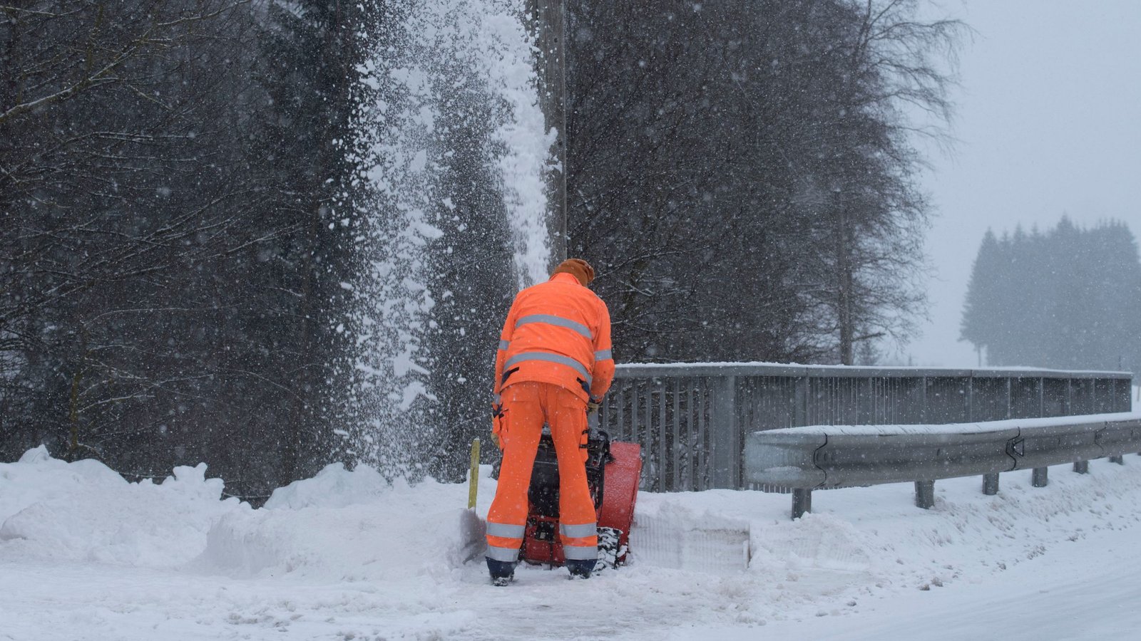 a professional wearing an orange suit removing snow using a snow removal machine